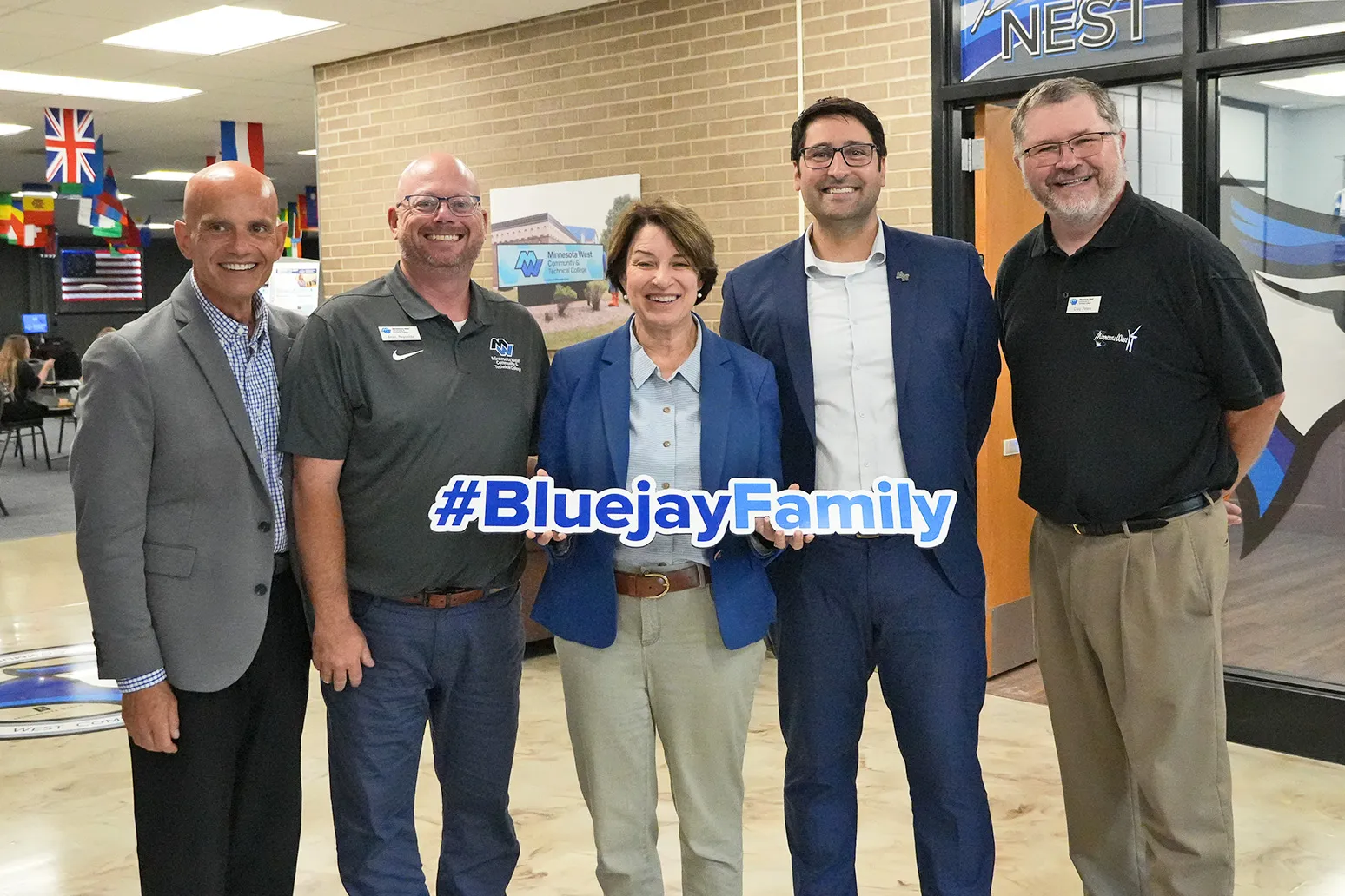 President Terry, Advisor Brian, Senator Amy Klobuchar, VP of Academic Affairs Daniel and Dean Craig standing with a Bluejay Family sign