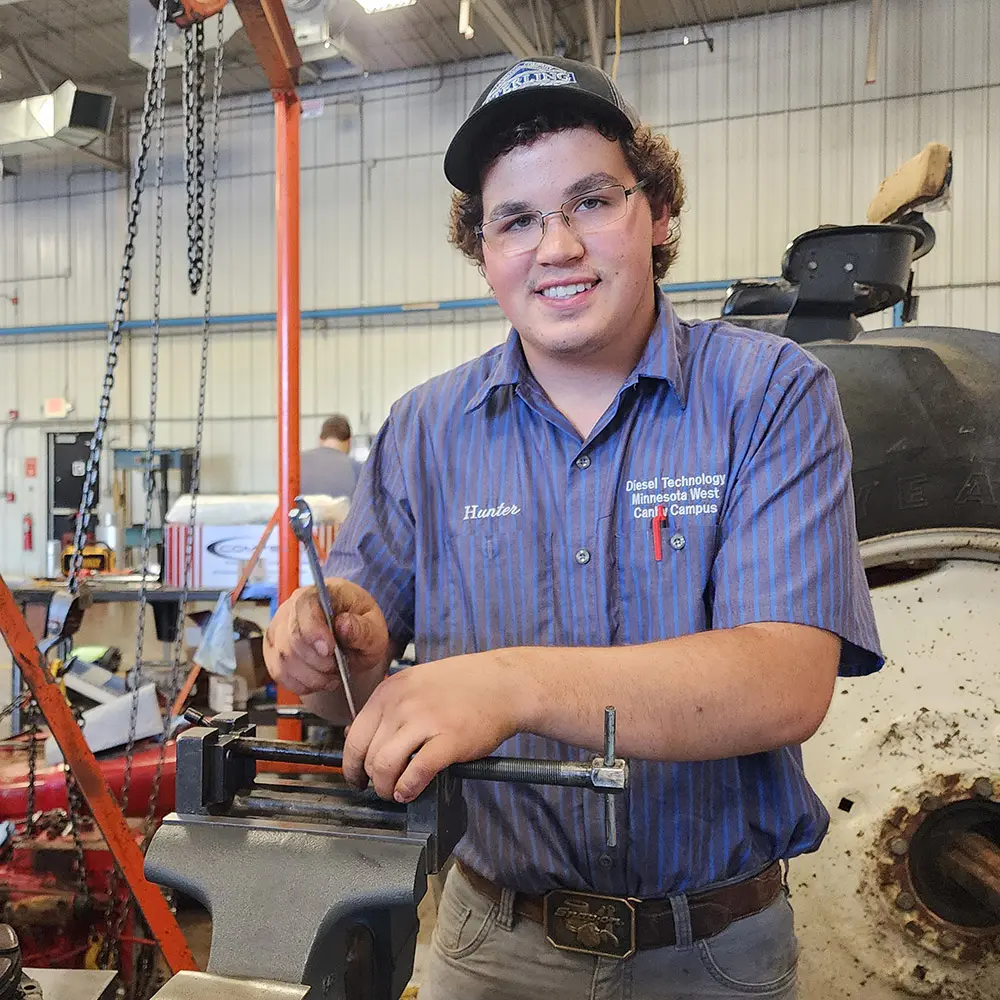 Hunter smiling while working on an engine in the Diesel building at the Canby Campus
